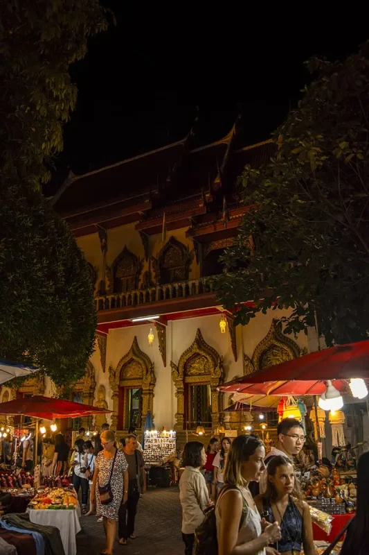 A serene night scene at a temple, with market stalls and visitors around it in Chiang Mai at the market