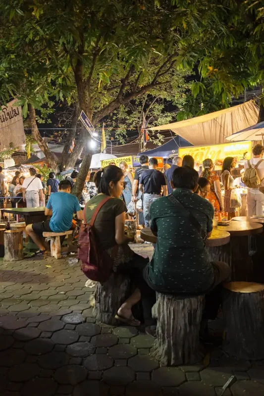Patrons enjoying street food under trees at the Sunday market in Chiang Mai