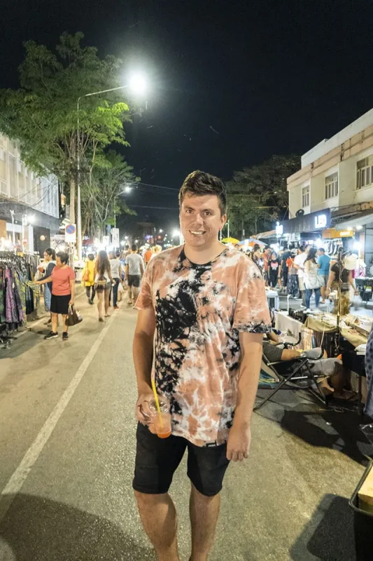 A happy market visitor holding a drink while standing in the middle of the lively market