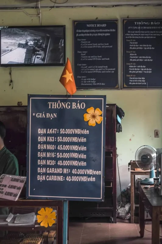 Best Cu Chi Tunnels Tours: Cheap VS Expensive 2025 12 Interior of a Cu Chi site displaying a board with prices for firing various guns, like AK47 and M16, reflecting the historical military aspect of the tunnels.