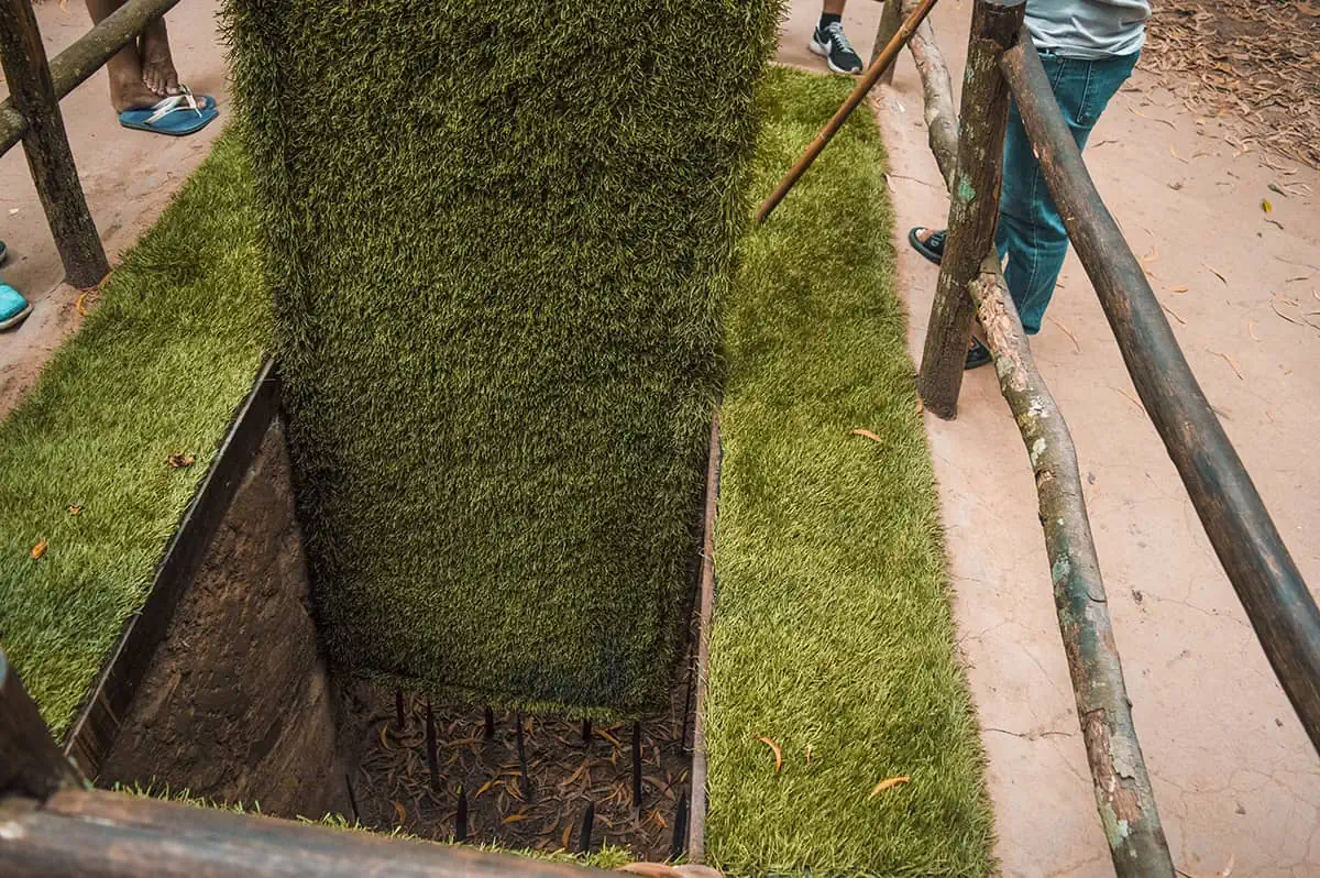 Best Cu Chi Tunnels Tours: Cheap VS Expensive 2025 13 A close-up view of a booby trap at the Cu Chi Tunnels, with sharp spikes at the bottom of a deep pit, surrounded by artificial grass to illustrate how traps were hidden during wartime.