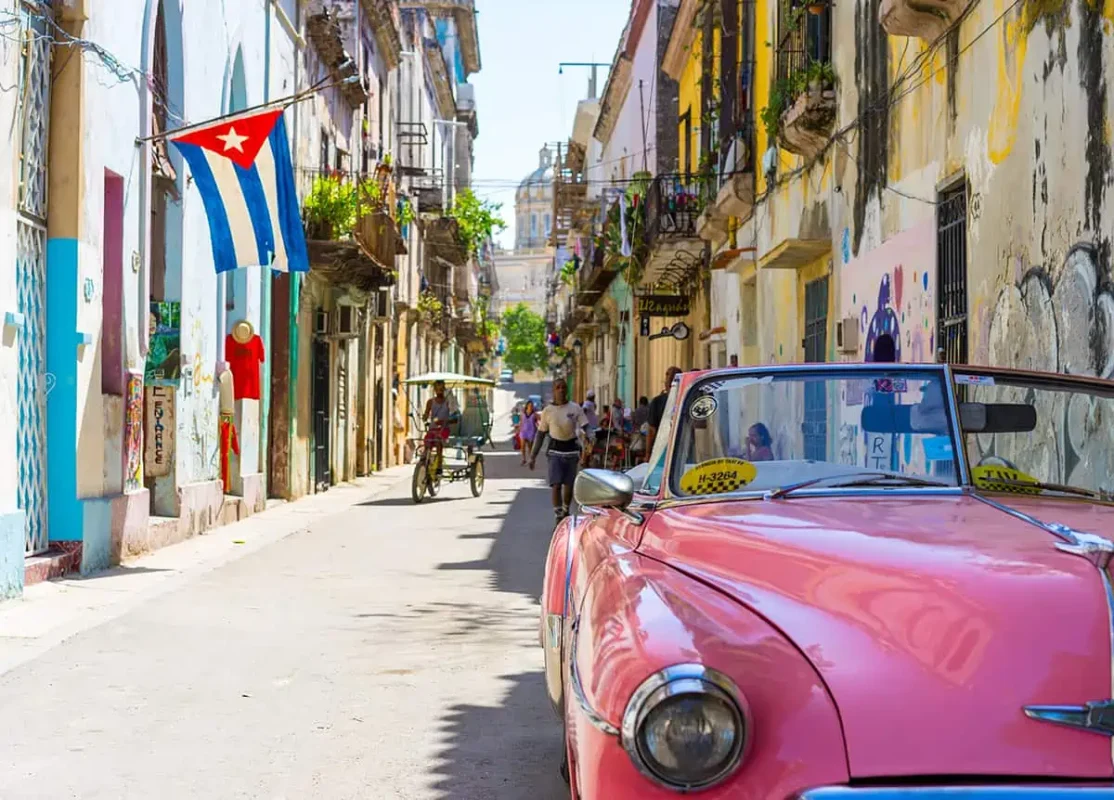 A classic pink car is parked on a narrow street in havana.