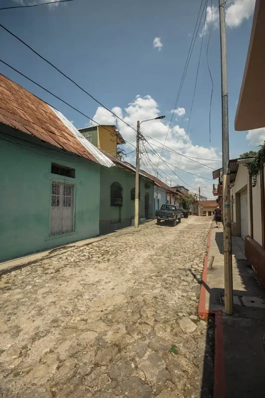 A quiet cobblestone street in Flores, lined with colorful houses and tangled overhead wires. The scene captures the rustic charm and tranquility of this small town.