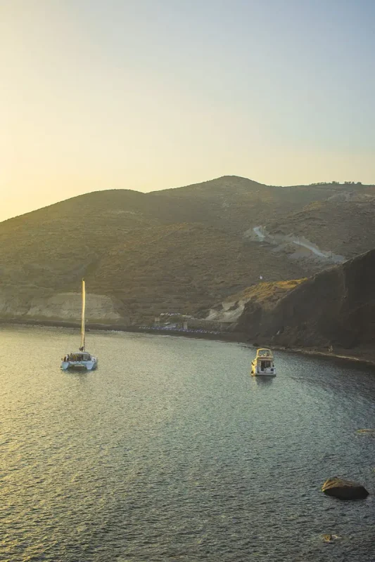 A group of sailboats in the water near a hill in santorini