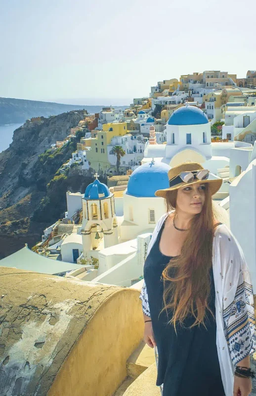 A woman in a hat standing in front of a village in santorini.