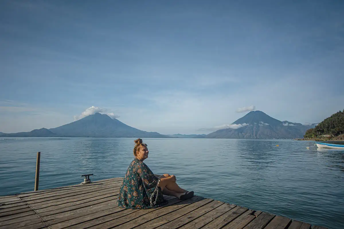 A woman sitting on a dock with volcanos in the background, enjoying the breathtaking natural scenery of lake atitlan