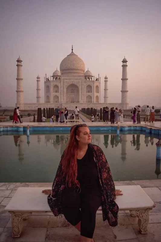 A woman sitting on a bench in front of the taj mahal.