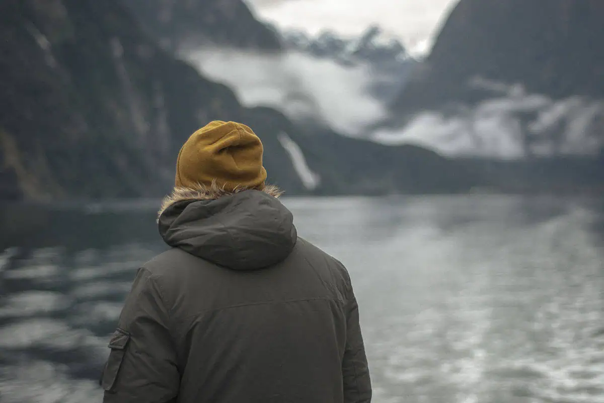 a man in a beanie looking out over the water towards Milford Sound’s mountains.