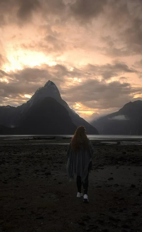 tasha amy walking towards Mitre Peak during a dramatic Milford Sound sunset.