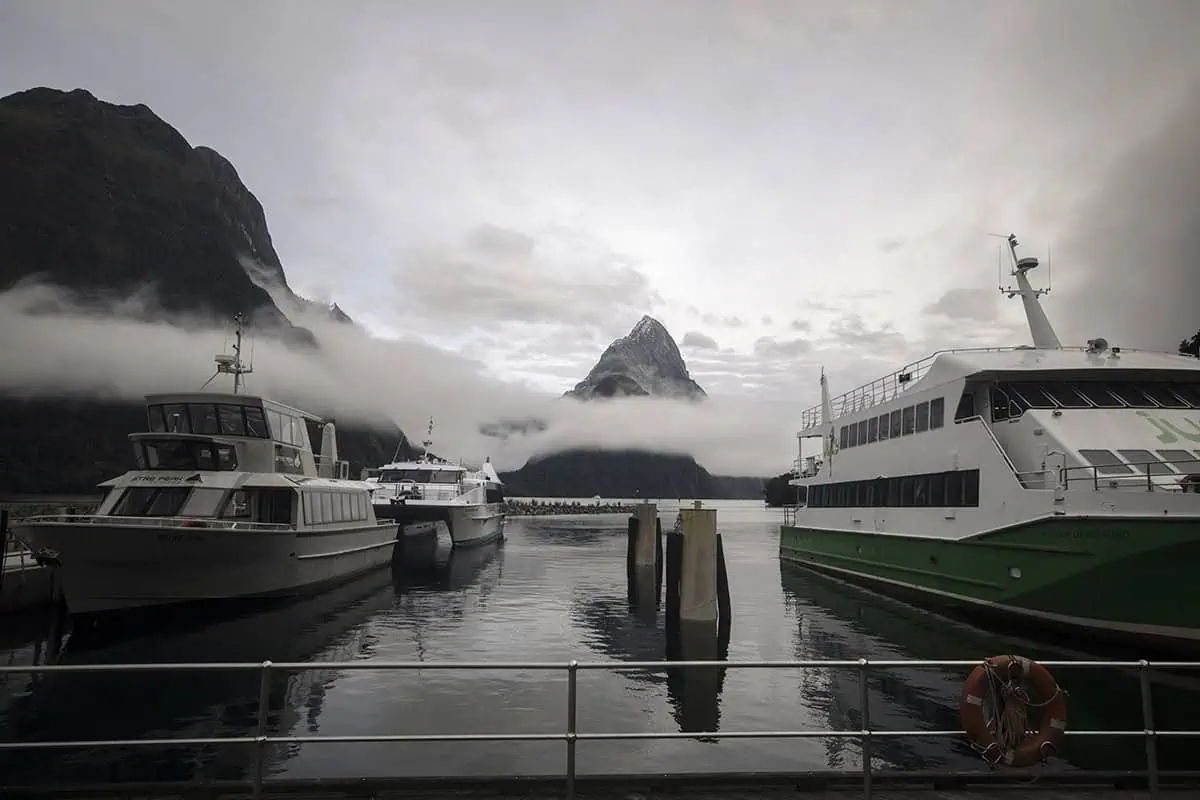 Tour boats docked up at the harbor in Milford Sound with Mitre Peak rising in the background.