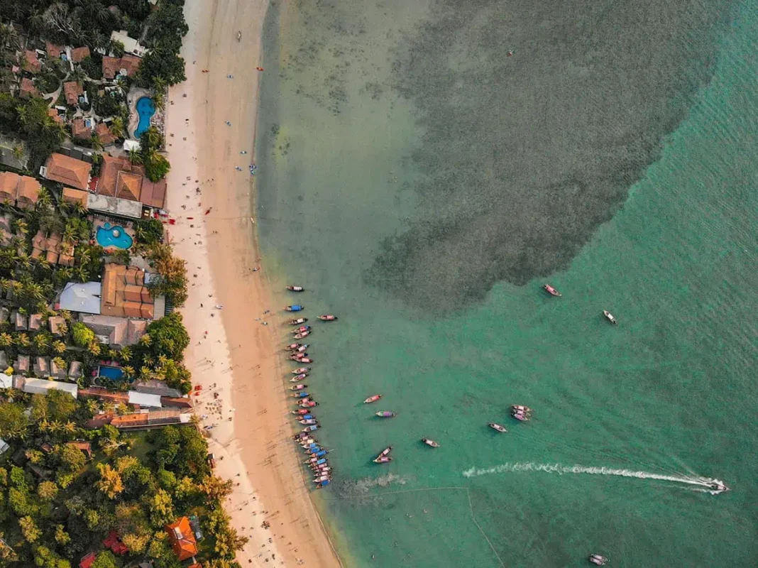 Is Railay Beach Closed: What You Need To Know (2025) 3 Aerial view of Railay Beach showcasing its sandy shore lined with boats, turquoise waters, and surrounding lush greenery. Though with the latest island shutdown is railay beach closed