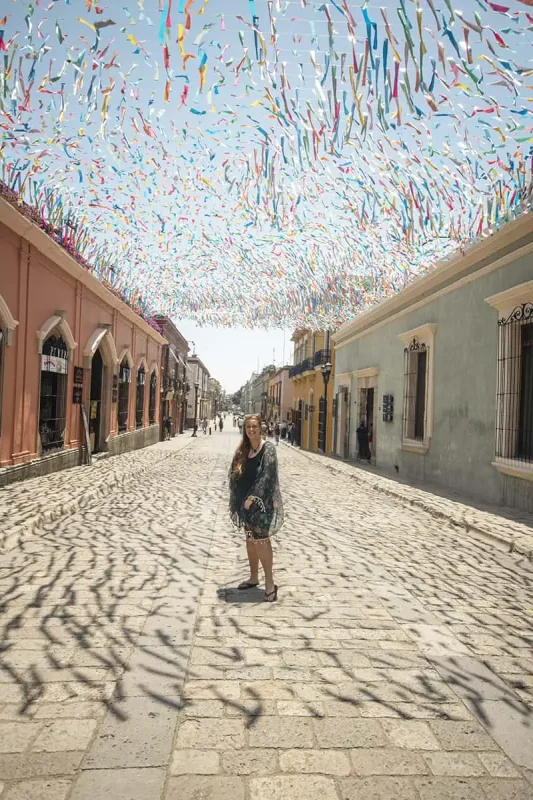 tasha amy standing in the middle of a cobblestone street with colorful streamers hanging above her