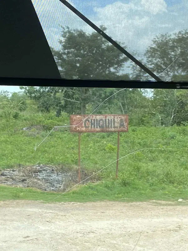 Mexico And Belize Itinerary: From 2 to 5 Weeks 13 A rusty sign reading "Chiquila" partially obscured by greenery, seen through a bus window, marking a point of interest on a Mexico and Belize itinerary.