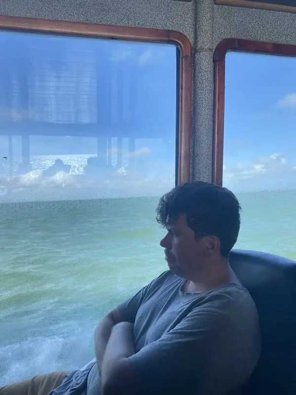 Mexico And Belize Itinerary: From 2 to 5 Weeks 21 A man sitting by the window inside a ferry, gazing out at the calm sea and clear sky. The reflection on the glass adds depth to the scene, portraying a peaceful and reflective travel experience.