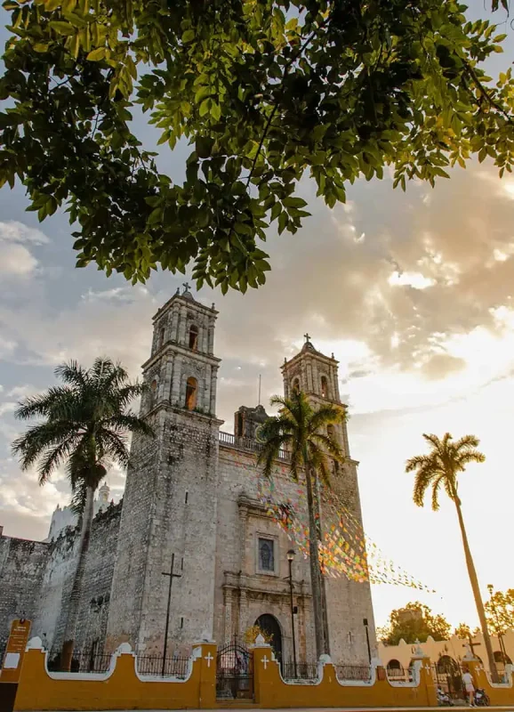 Mexico And Belize Itinerary: From 2 to 5 Weeks 14 Historic cathedral with twin bell towers framed by palm trees and lush green leaves in Valladolid, Mexico. The late afternoon sun casts a warm glow on the stone facade, capturing the architectural beauty and cultural richness of the region.