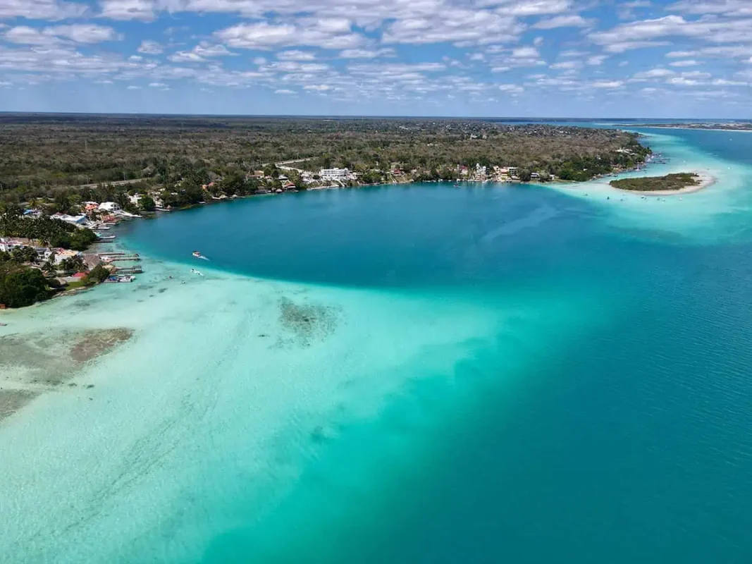 Mexico And Belize Itinerary: From 2 to 5 Weeks 29 Aerial view of a serene, blue lagoon with a gradient of shallow to deep waters surrounded by lush greenery in Bacalar. The lagoon's calm, clear waters create a peaceful and idyllic setting, perfect for a refreshing swim or relaxation