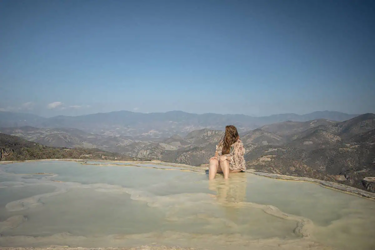 Mexico And Belize Itinerary: From 2 to 5 Weeks 51 Tasha Amy sitting at the edge of a natural infinity pool, dipping her feet into the water while gazing at the expansive mountainous landscape. The clear sky and distant hills provide a breathtaking view.