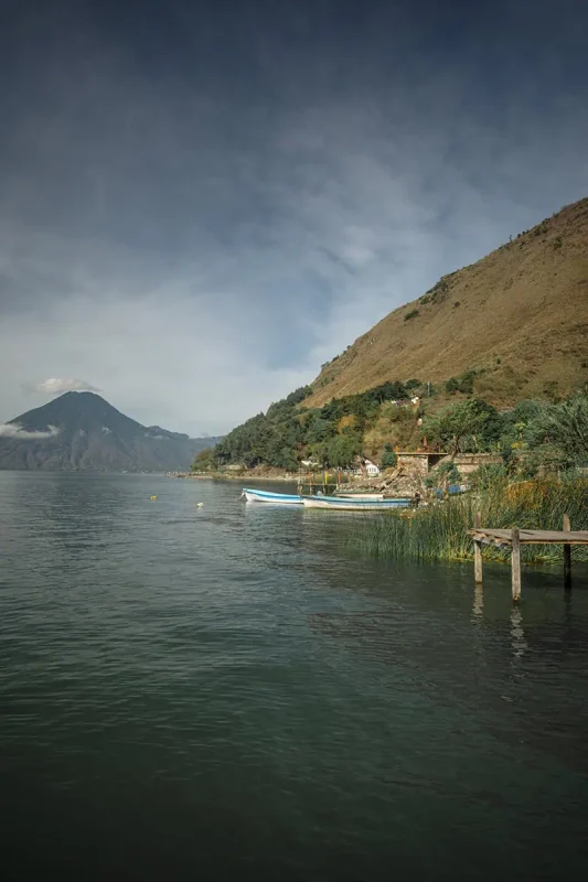 Lake Atitlán with several boats moored along a pier, set against a backdrop of green hills and a calm lake.