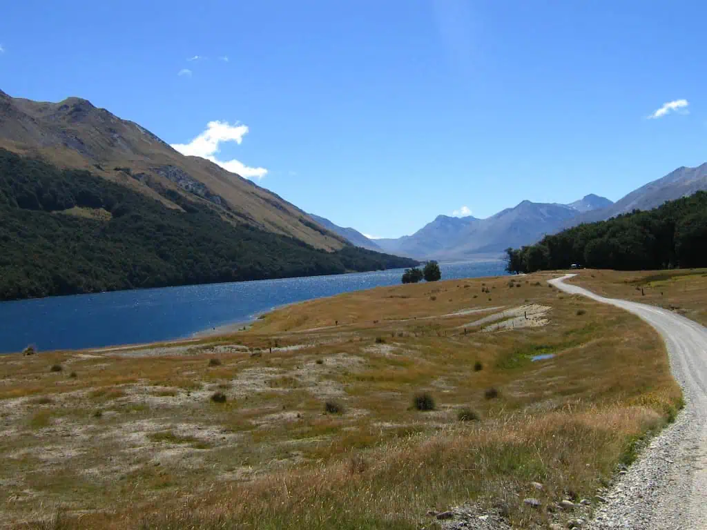 A winding gravel road curves past Mavora lake toward distant mountains, one of the lord of the rings filming locations in fiordland