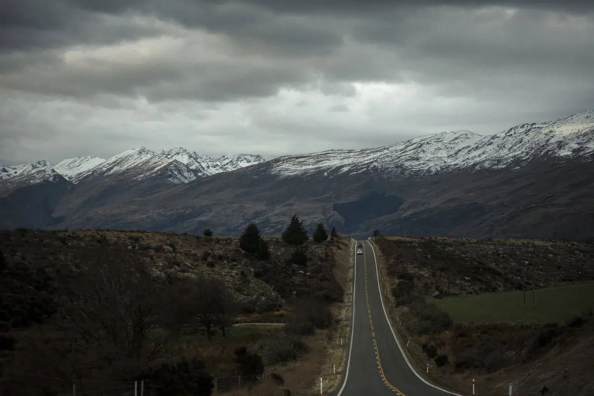 A long straight road leads into a valley of rugged mountains dusted with snow in fiordland