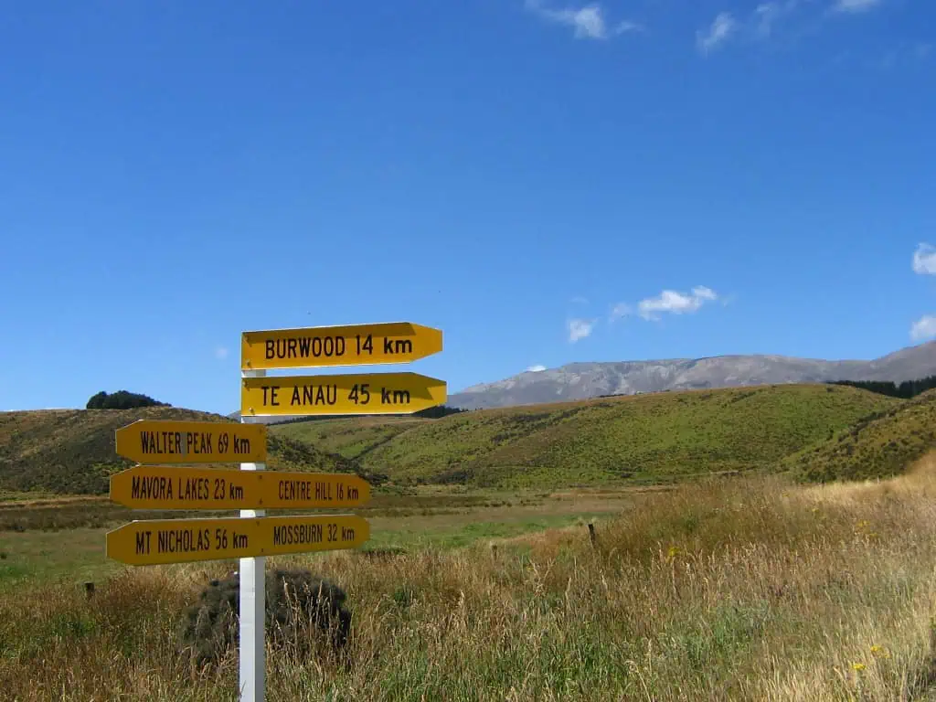 A yellow road sign points to destinations including Te Anau, Mavora Lakes, and Walter Peak, some of the Lord of the Rings filming locations in New Zealand.