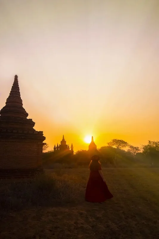 tasha amy in a red dress walks through a field of pagodas at sunset.