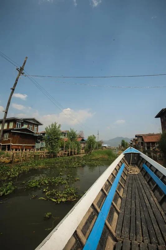 The back of a boat on a canal in Myanmar with houses in the background.