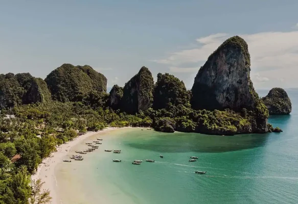 Aerial view of Railay Beach with traditional longtail boats taking people from ao nang to railay beach, and limestone formations covered in jungle.