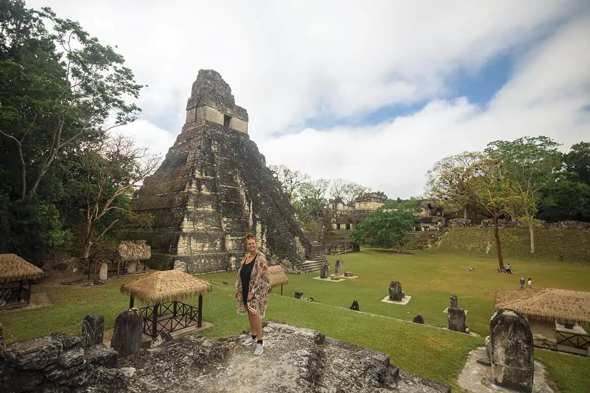 Tasha Amy gazing at the iconic Temple I at Tikal National Park, a popular destination for day trips from San Ignacio, with thatched-roof structures dotting the landscape.