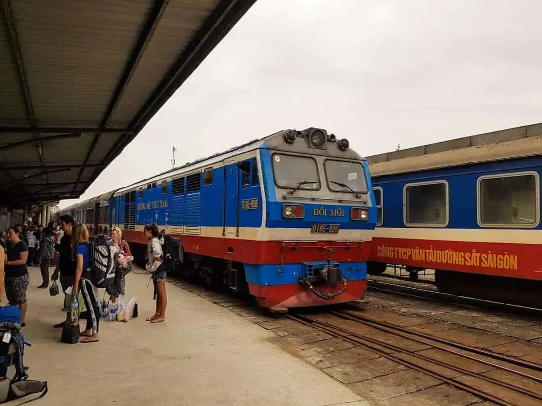Passengers boarding a blue and red train at the station, preparing for an overnight journey through vietnam