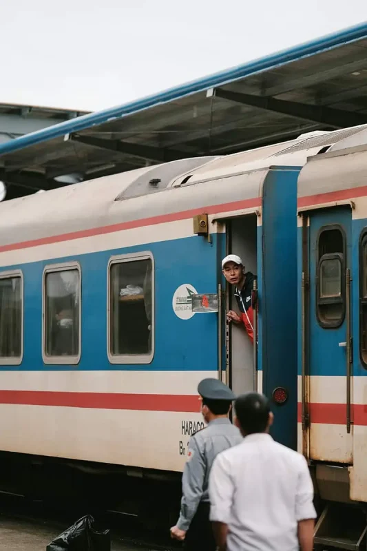 Train staff member looking out from the door of a sleeper train in Vietnam, ready to assist passengers.