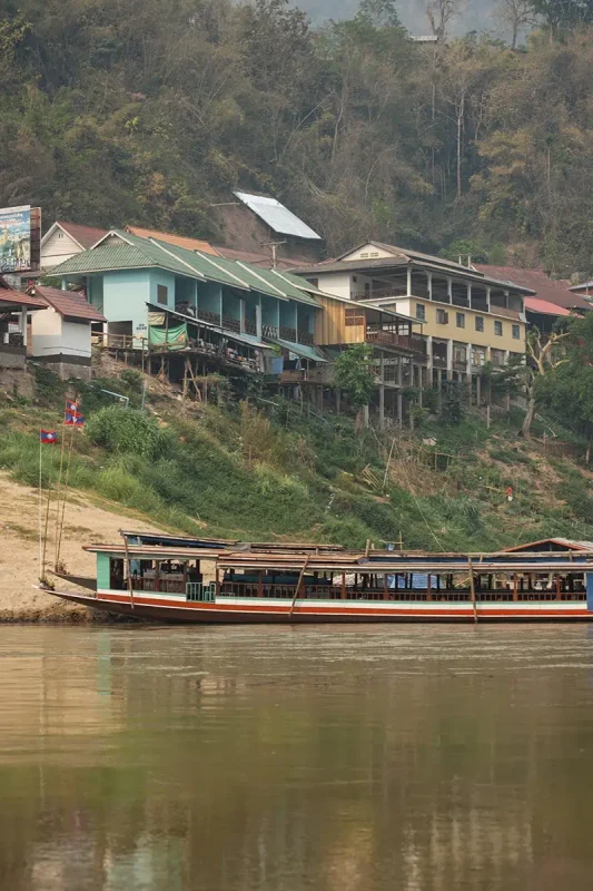A slow boat on the river against a backdrop of colorful houses.