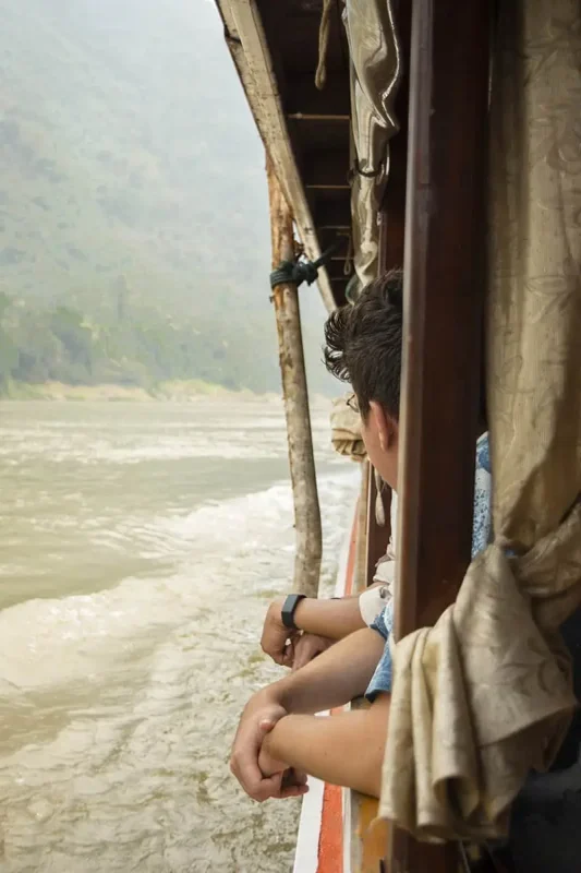 A traveler looks contemplatively at the rushing waters of the Mekong River from the side of a boat