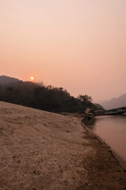 The golden hour illuminates the serene Mekong River beside a sandy bank