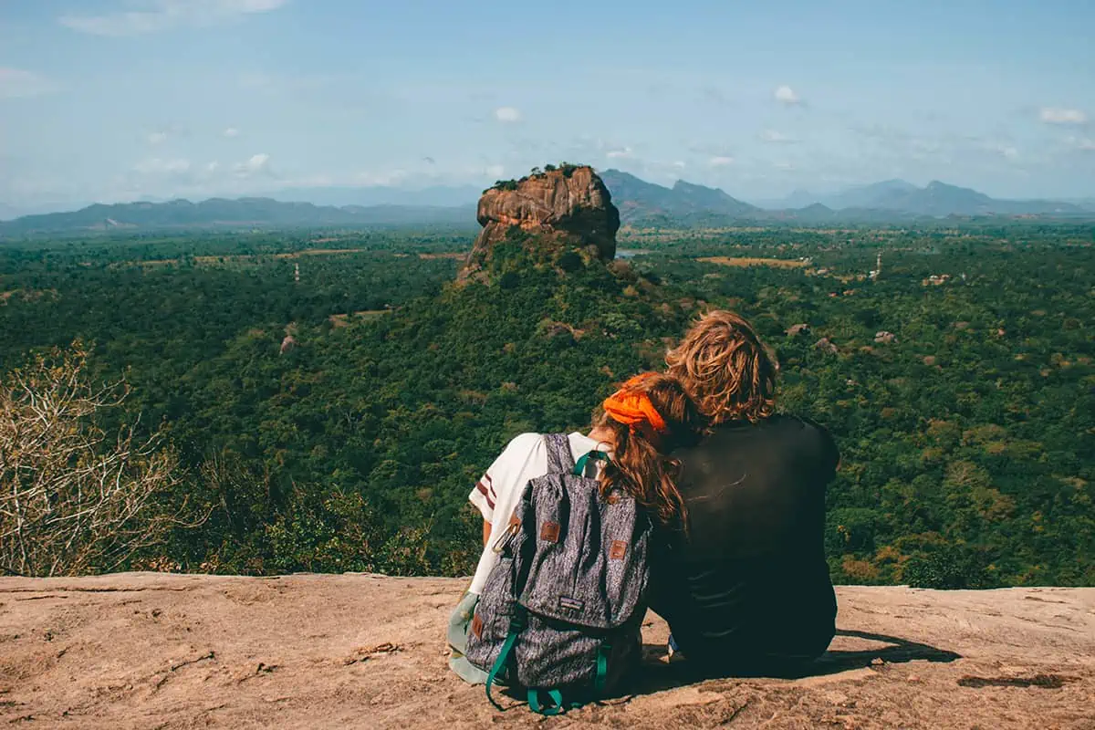 Two people sitting on top of a rock overlooking sri lanka.