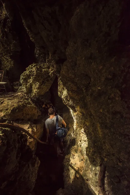 14 BEST Things To Do In Lifou: Cruise Passengers & More 15 A person descending into a dark, rugged cave, an adventurous activity for travelers exploring the hidden natural wonders of Lifou, New Caledonia.