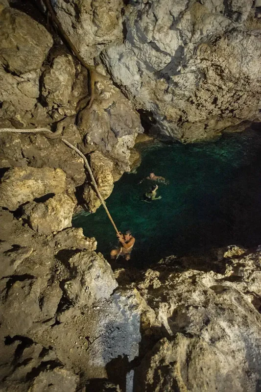 14 BEST Things To Do In Lifou: Cruise Passengers & More 18 An individual using a rope to descend into a crystal-clear natural pool inside a cave, offering a unique swimming experience in Lifou.