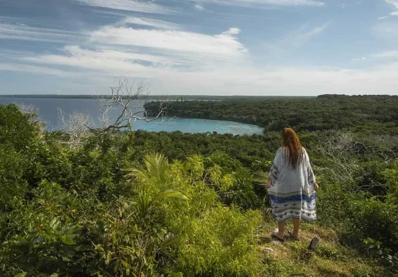 A person standing at the edge of a lush overlook, gazing out at a secluded bay in Lifou, New Caledonia, showcasing one of the serene things to do in Lifou.