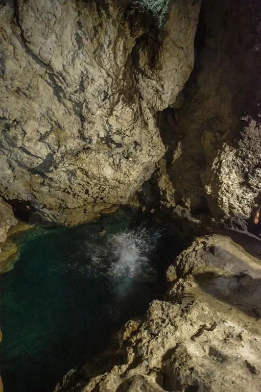 14 BEST Things To Do In Lifou: Cruise Passengers & More 17 A person jumping into a luminous blue natural pool within a cave, a hidden gem and one of the exhilarating things to do in Lifou from a cruise ship.