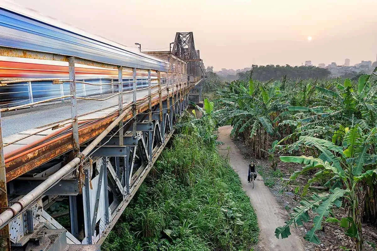 Long exposure capturing the motion of a Vietnam train on a bridge over lush greenery at sunset