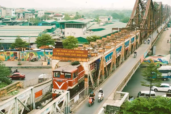 Elevated view of a first-class sleeper train in Vietnam traveling over a graffiti covered bridge