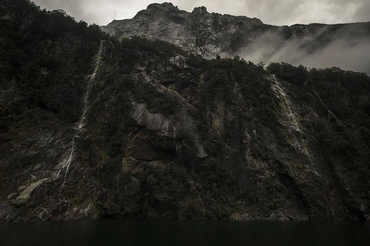 multiple waterfalls at four sisters falls descend from the mountain under a cloudy sky in Milford Sound