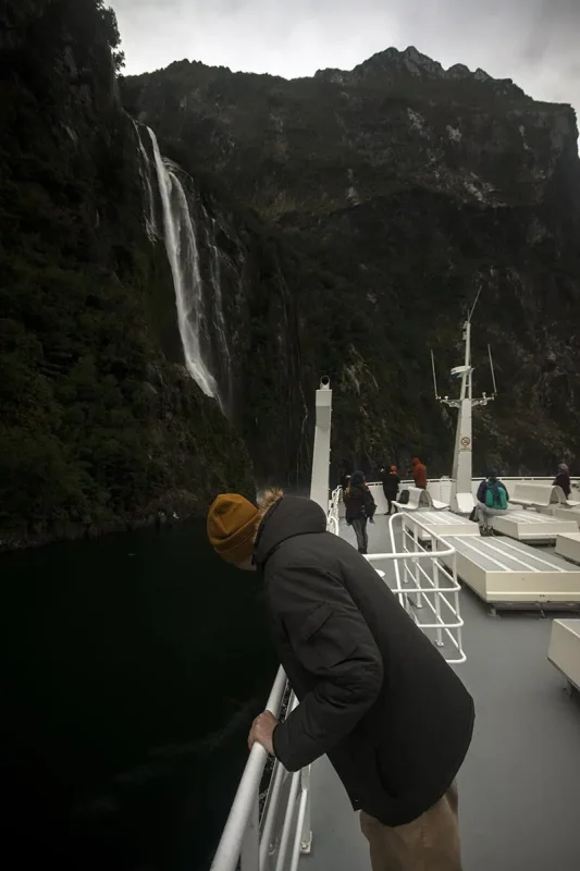 A person on a boat leans over the railing as the vessel approaches stirling waterfalls in Milford Sound