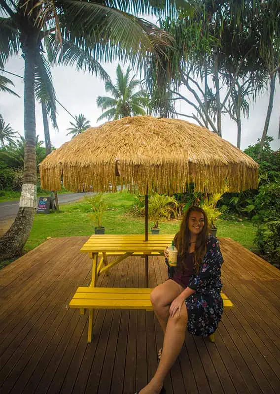 Where To Eat In Rarotonga: BEST Restaurants & Cafes 2025 11 tasha amy enjoying a leisurely break under a thatched umbrella at a scenic outdoor seating area, typical of the best restaurants in Rarotonga.