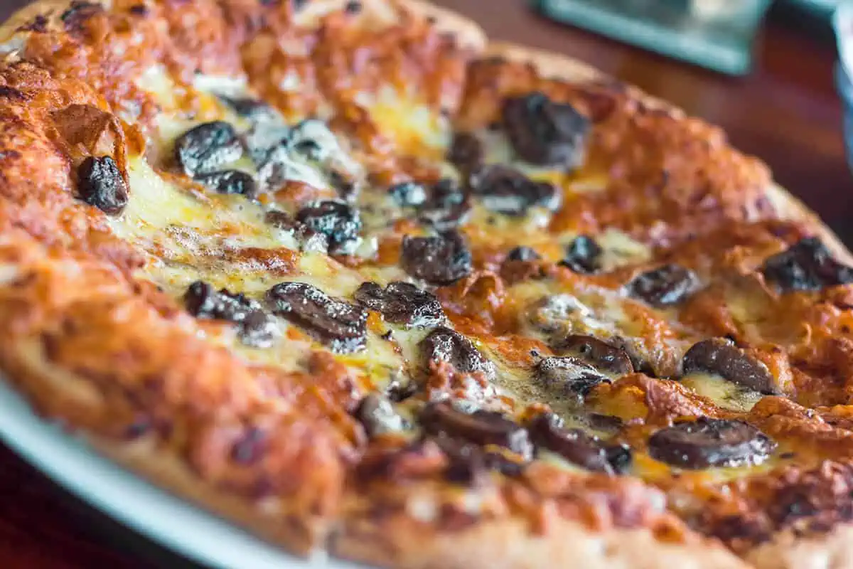Where To Eat In Rarotonga: BEST Restaurants & Cafes 2025 23 Golden-brown mushroom pizza on a white plate from Trader Jacks, showcasing the flavors of Rarotonga restaurants, ideal for a relaxed dining experience