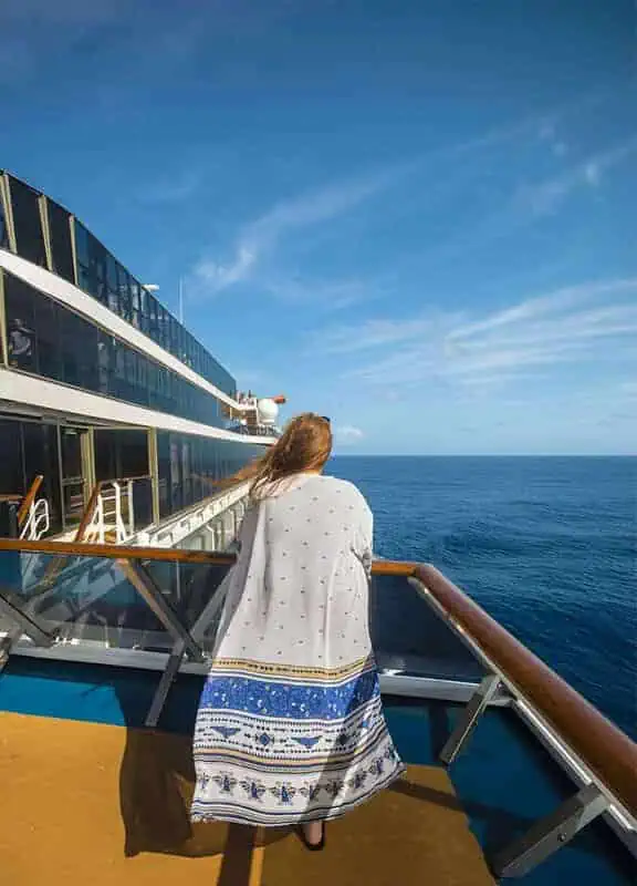 120+ Would You Rather Travel Questions For Ultimate Wanderers 4 tasha amy stands at the ship’s railing under a blue sky, looking toward the sea with waves stretching into the distance.